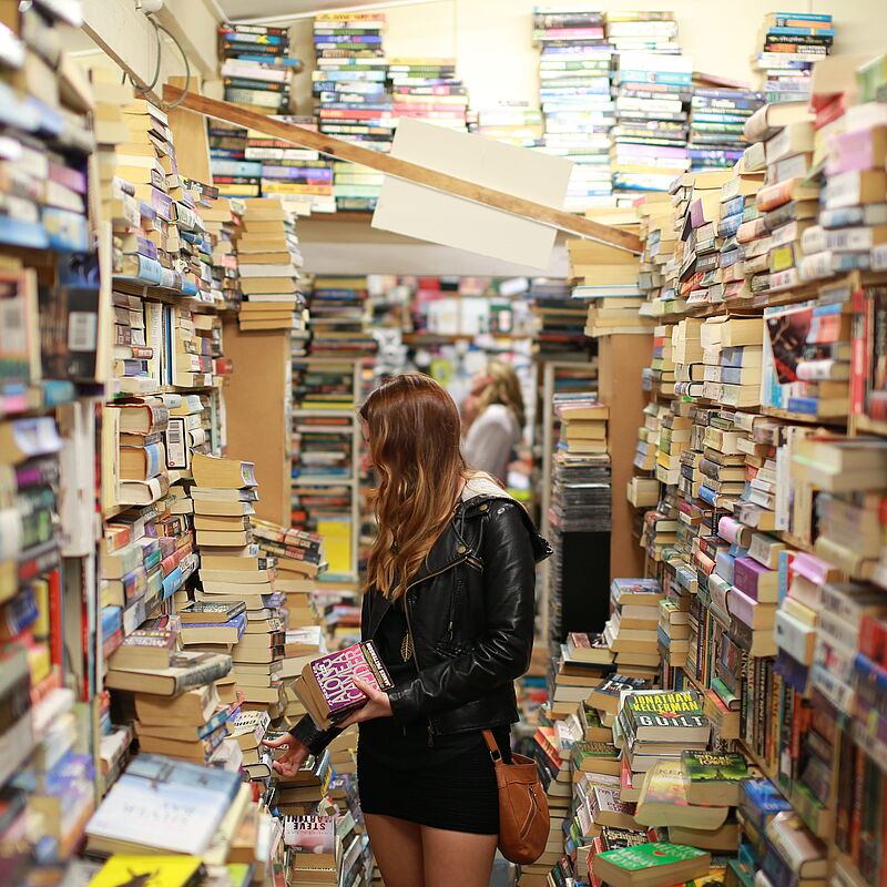 Eine Frau steht in eine Buchladen und stöbert in den Stapeln.