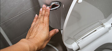 Eine Frauenhand, die eine Toilettenspülung drückt.. Weitere Informationen siehe Bildunterschrift