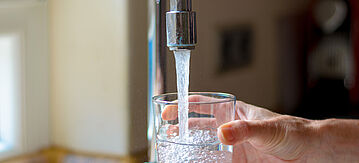 Eine Hand hält ein Glas unter den Wasserhahn in der Küche.