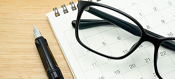 Brille auf einem Kalender daneben ein Kugelschreiber