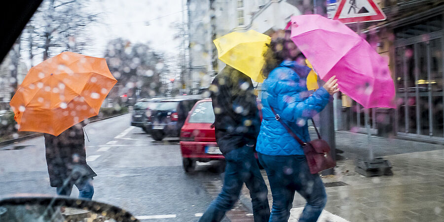 Menschen mit Regenschirmen überqueren eine Straße