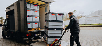 Eine Person lädt einen LKW mit Mehrweg-Transportkisten aus Kunststoff voll.