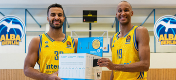 2 Alba-Spieler in einer Basketball-Halle halten einen Karton für alte Smartphones.