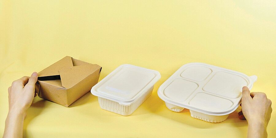 Drei Verpackungen für Essen zum Mitnehmen vor einem gelben Hintergrund