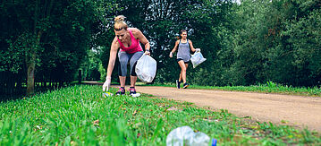 Zwei Frauen sammeln beim Joggen Müll auf.