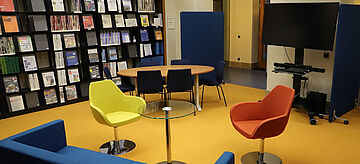 Blick in die MIZ Bibliothek des Bundesumeltministeriums; Bücherregal, blaue Couch und ein gelber und orangener Stuhl. 