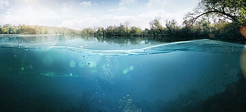 Die Kamera ist halb unter Wasser. Man sieht den blauen See und das grüne Ufer.. for further information see image caption