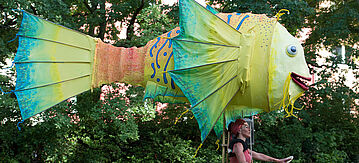 Eine Frau führt einen Flugdrachen in Form eines Fisches vor