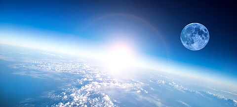 Blick auf die Erde, dahinter geht die Sonne auf und erleuchtet den blauen Planeten.