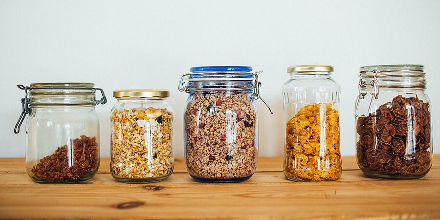 Fünf Vorratsgläser mit verschiedenen Sorten von Müsli auf einem Holztisch