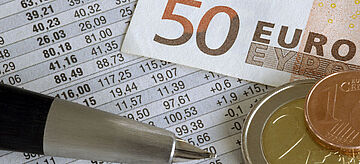 Geldschein, Münzen und ein Stift liegen auf Abrechnungsdokument