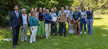 Gruppenfoto. Im Bild von links nach rechts: Ivo Reßler – Bürgermeister Stadt Lorch Dr. Anke Höltermann – Bundesamt für Naturschutz Angelika Balzert (vorne) – Bundesumweltministerium Claudia Steinacker – Bundesamt für Naturschutz Christian Dittmann – hess. Landwirtschafts- und Umweltministerium (hintere Reihe) Christina Uhl – hess. Landwirtschafts- und Umweltministerium Dr. Jürgen Willig – hess. Landwirtschafts- und Umweltministerium (hintere Reihe) Parlamentarische Staatssekretärin Dr. Bettina Hoffmann – BMUV Carsten Wilke – hess. Landwirtschafts- und Umweltministerium (hintere Reihe) Jan Stetter – Forstamt Rüdesheim (Hessen-Forst) Gunter Schöcker – Obere Naturschutzbehörde Regierungspräsidium Darmstadt Nico Eidenmüller – ZGF-Projektleiter des Wispertaunus Großprojekts Moritz Kraus – Obere Forstbehörde Regierungspräsidium Darmstadt Ramona Divivier – Naturpark Rhein-Taunus Dr. Christof Schenk – ZGF Geschäftsführer Volker Diefenbach – Bürgermeister Gemeinde Heidenrod Lucy Fleischhauer – ZGF Katharina Sabry – hess. Landwirtschafts- und Umweltministerium
