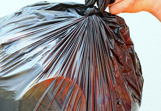 Eine Person wirft einen Müllbeutel in die Mülltonne. 