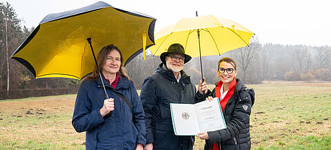 Amtsleiterin für Landwirtschaft und Naturschutz beim Landratsamt Böblingen Yvonne Bäuerle, Erster Beigeordneter der Stadt Weil der Stadt Jürgen Katz und Rita Schwarzelühr-Sutter unter Regenschirmen mit Förderbescheid