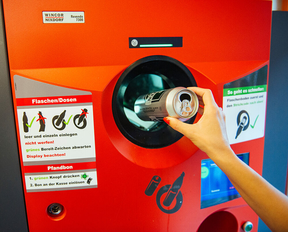 Person wirft eine Dose in einen Pfandautomaten