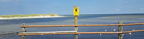 Blick aufs Wasser hinter einem Holzgelände und Naturschutz Schild