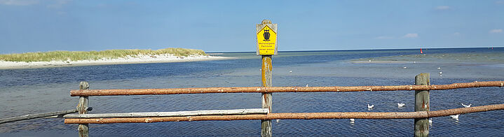 Blick aufs Wasser hinter einem Holzgelände und Naturschutz Schild