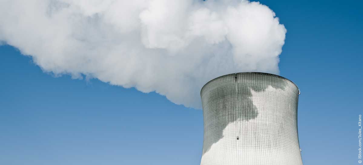 Kernkraftwerk mit dampfendem Turm vor dem klaren blauen Himmel.